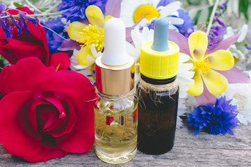 essential oil with a rose in a glass bottle near wildflowers on wooden background.