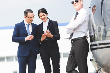 businesspeople using smartphone near pilot and helicopter