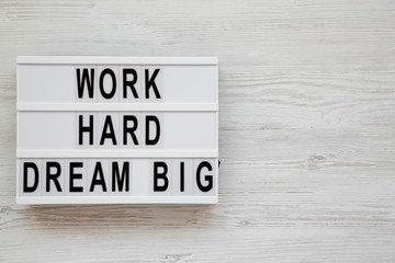 'Work hard dream big' words on a lightbox on a white wooden surface, top view. Flat lay, overhead, from above. Space for text.