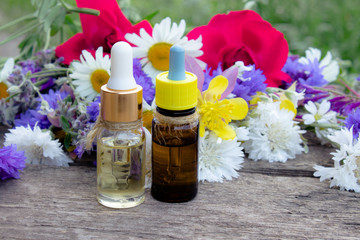 Natural essential oil with wild flowers on wooden background.