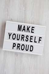 Modern board with text 'Make yourself proud' on a white wooden surface, top view. Flat lay, overhead, from above.