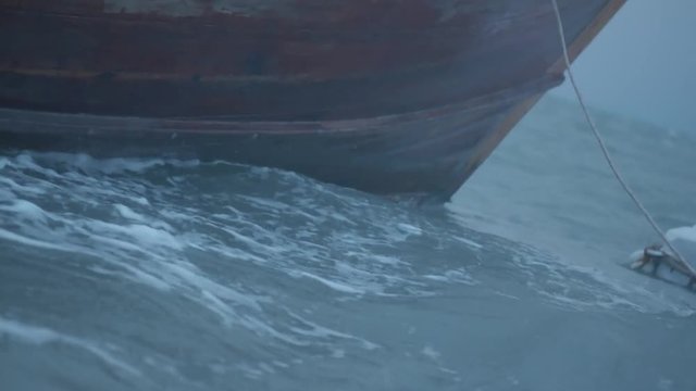Closeup boat bow drifting in the wavy sea over cloudy dark sky background. Cinematic dramatic footage of boat in restless sea water and sky before the storm in early morning