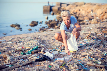 Woman collect garbage on the beach. Environmental pollution concept