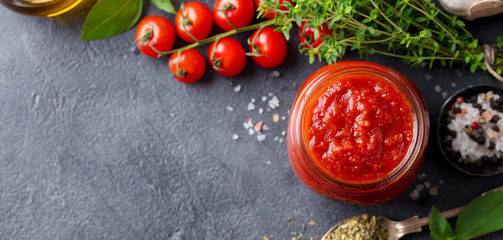 Traditional tomato sauce in a glass jar with herbs, tomatoes and olive oil. Top view. Copy space. Slate background.