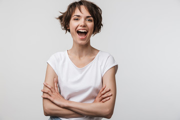 Image of young woman in basic t-shirt smiling at camera while standing with arms crossed