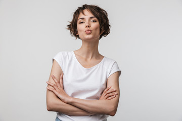 Image of happy woman in basic t-shirt looking at camera while standing with arms crossed