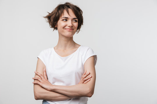 Image of optimistic woman in basic t-shirt smiling and looking aside while standing with arms crossed