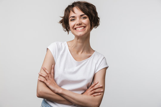 Image of cheerful woman in basic t-shirt smiling at camera while standing with arms crossed