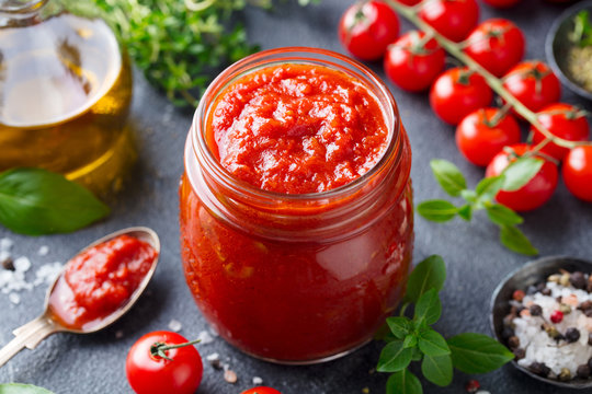 Traditional tomato sauce in a glass jar with fresh herbs, tomatoes and olive oil. Copy space. Slate background.