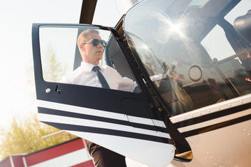 handsome Pilot in formal wear and sunglasses opening door of helicopter
