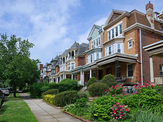 Row of large old brick houses with front porches and gardens