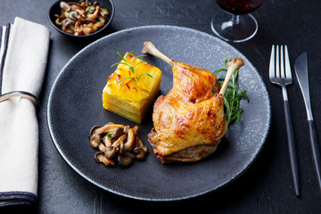 Duck legs confit with potato gratin and mushroom on a plate. Slate background.