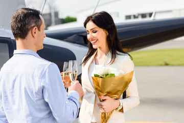 husband and wife clinking champagne glasses on romantic date near helicopter