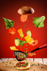 Cooking hamburger with flying tomatoes, cheese and herbs