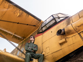A handsome young pilot sitting on the wing of a plane
