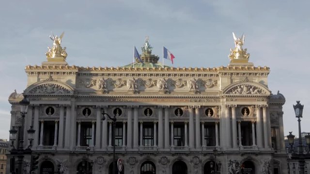 Parisian monument at Opera place in wide shot. Gold statue historical sculptures with french flag fluttering in the wind with beautiful blue sky during summer afternoon in Paris.