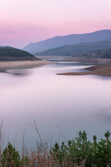 Soft, colorful, blue hour view of meandering Zavoj lake with rafts parked on the steep bank and distant horizon mountains