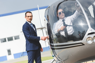 Pilot in formal wear sitting in helicopter while businessman looking at camera