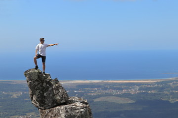 ISOLATED BOY POINTING FROM THE TOP OF A ROCK NEAR THE OCEAN ON SUMMER HOLIDAY