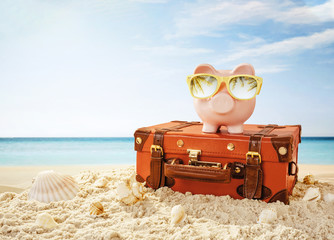 Piggy bank wearing sunglasses resting on the tropical beach with copy space