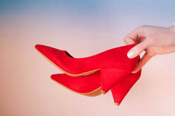 Woman holding coral red high heels in hand on blue background.