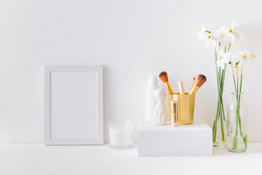 Home interior with decor elements. White frame, white daffodils in a vase, cosmetic set