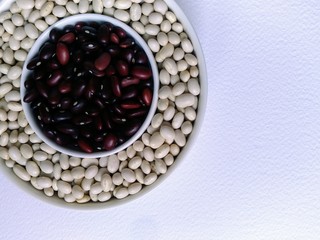the reddish brown beans in a small white Cup are framed by white beans in a larger bowl. items are located in the corner of the image. top view, foodfoto, mock up, text space, flat layout. on light ba