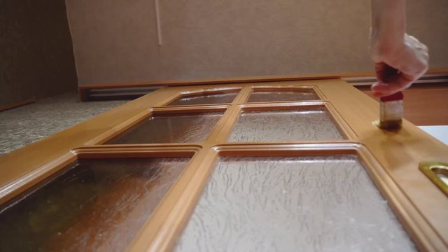 An elderly woman in the apartment makes repairs. Paints, varnishes wooden doors. Brush. smear.