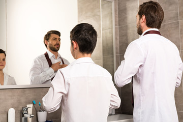 father and son dressing in formal wear in front of mirror in bathroom