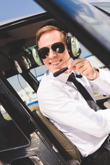 handsome smiling Pilot in sunglasses and headset sitting in helicopter cabin