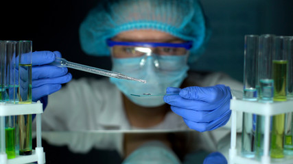 Scientist dripping oily liquid on test glass, conducting experiment, laboratory