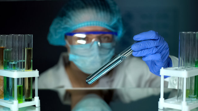 Lab worker looking at tube with blue liquid, detergents, perfumery production