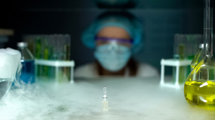 Ampule with transparent liquid in refrigerator in front of researcher, pharmacy