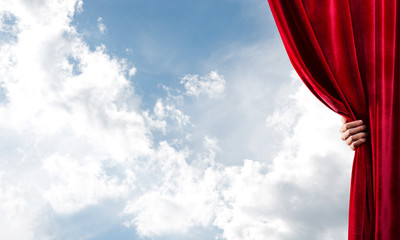 Cloudy landscape behind red curtain and hand holding it