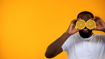 Funny African-American man clothing eyes with half of oranges, healthy lifestyle