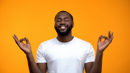 Smiling Afro-American man meditating against yellow background, yoga exercise