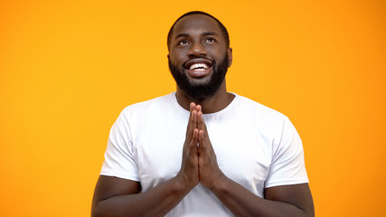 Happy African-American man holding hands for pray and looking up, blessing god