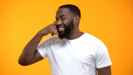 Cheerful Afro-American man showing call me gesture, getting acquainted on party