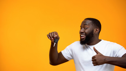 Excited Afro-American man holding car key and showing thumbs up, purchase