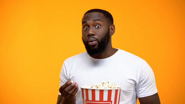 Excited African-American male with popcorn watching interesting TV program