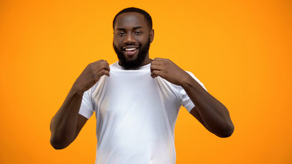 Smiling black man showing his white T-shirt isolated on yellow background