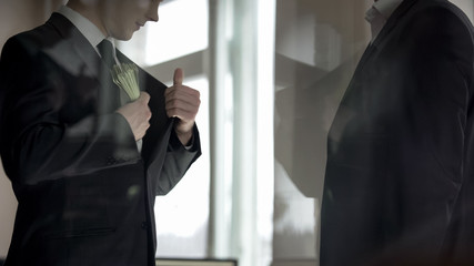 Businessman hiding money in suit jacket, two partners sharing business profit