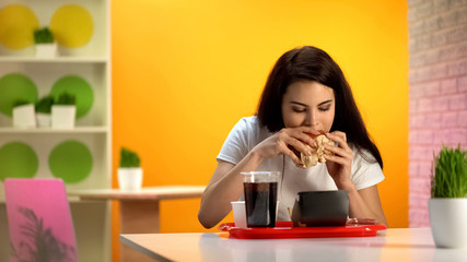 Beautiful lady biting tasty cheeseburger, sweet soda beverage standing on table