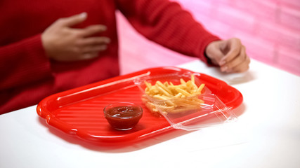 Woman feeling stomach pain, french fries with ketchup on table, acid indigestion