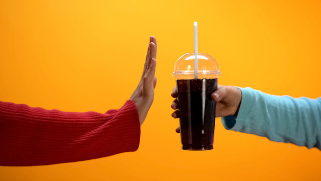 Lady showing stop gesture to soft drink on bright background, sugar overweight