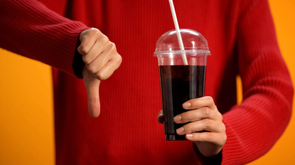 Woman with soft drink glass showing thumbs down, sweet beverage disapproval