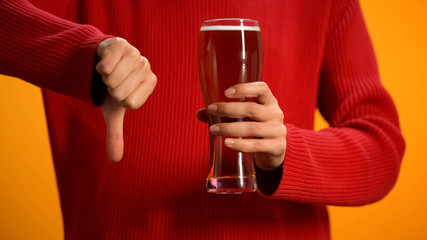Woman holding glass of beer showing thumbs down, drunk driving danger, alcohol