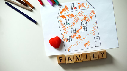 Family word on cubes lying near heart sign and kids house drawing, orphan