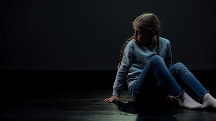 Lonely girl sitting in dark room and looking around, orphan waiting family