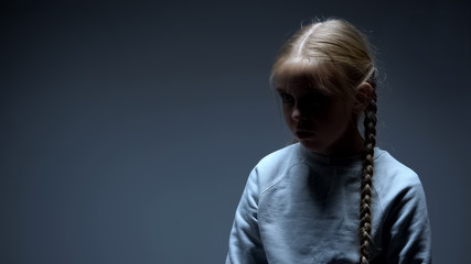 Unhappy little girl standing alone in darkness, bullying and violence victim